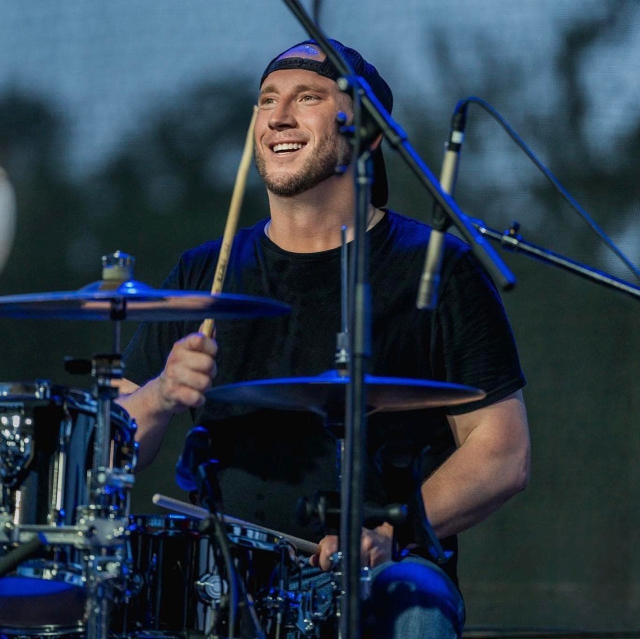 Rob Milligan smiling while playing drums onstage
